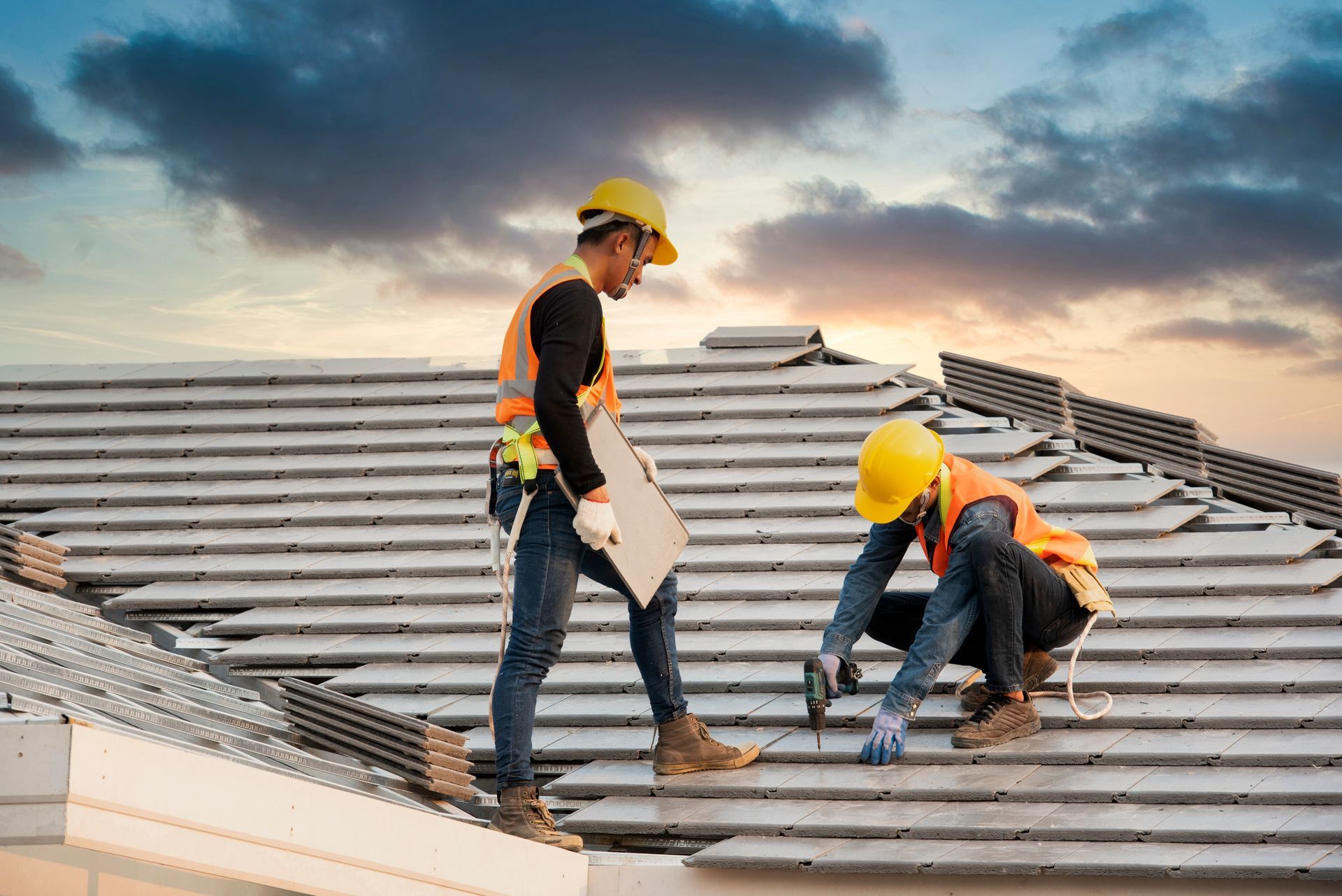 A skilled local roofing contractor secures gray concrete roof tiles with a drill. A skilled local roofing contractor secures gray concrete roof tiles with a drill.