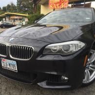 Black BMW sedan parked outdoors, front view with a visible license plate and wet pavement.