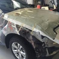 Damaged gray car fender wrapped in plastic inside an auto repair shop