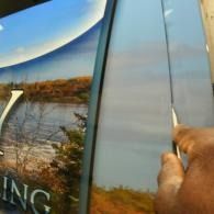 Hand pulling open a car door, revealing a scenic lake and autumn landscape reflected on the window