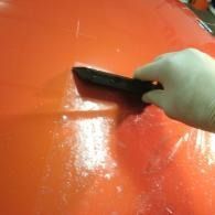 Hand holding a black squeegee scraping water across a glossy orange surface