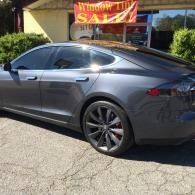 Gray sedan parked outside a window tint shop sign in bright sunlight