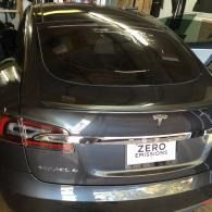 Rear view of a gray Tesla sedan with a “Zero Emissions” license plate in a garage