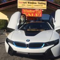 White BMW with butterfly doors open in front of window tinting sale signs
