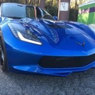 Blue sports car parked outdoors, front view on a gravel driveway.
