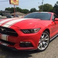 Red Ford Mustang with white racing stripes parked outdoors on a sunny street