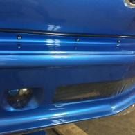 Close-up of a blue car front bumper with a round fog light and lower grille opening