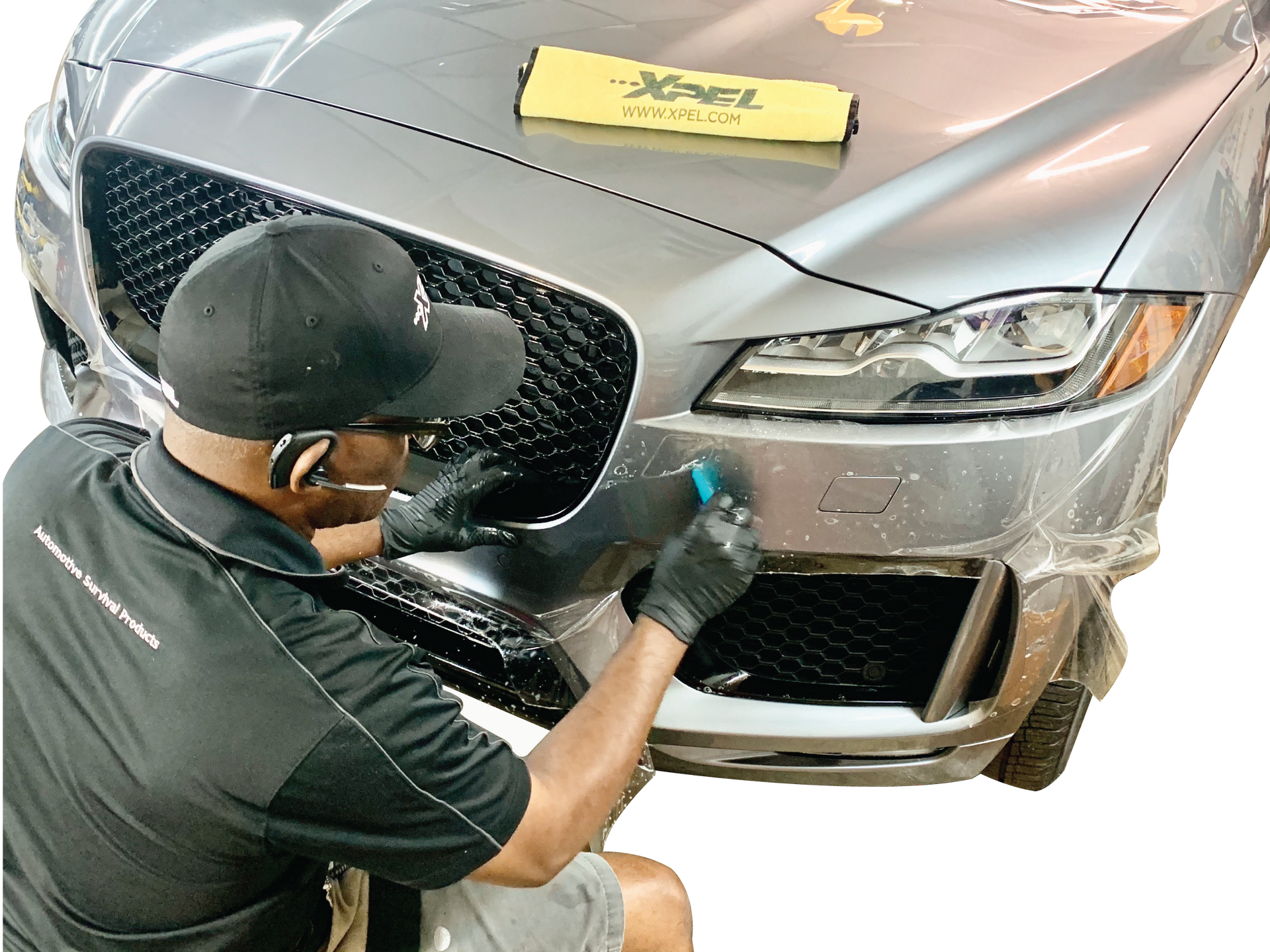 Mechanic polishing the front bumper of a silver car with a yellow cloth on the hood