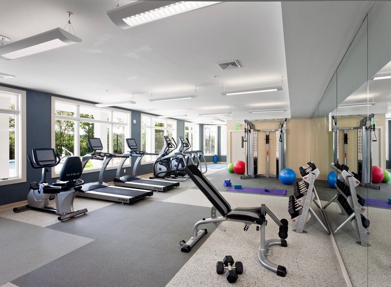 Indoor fitness center with cardio machines, free weights, and a mirrored wall.