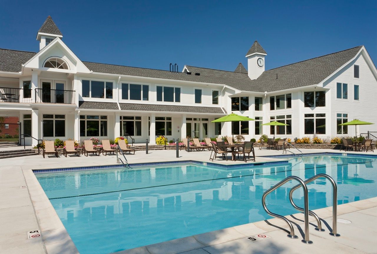 Outdoor pool area at a residential community with lounge chairs and a white clubhouse.