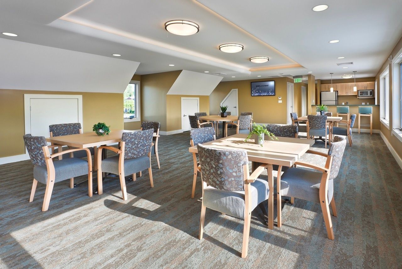Bright community lounge with multiple tables and upholstered chairs in a shared dining area.