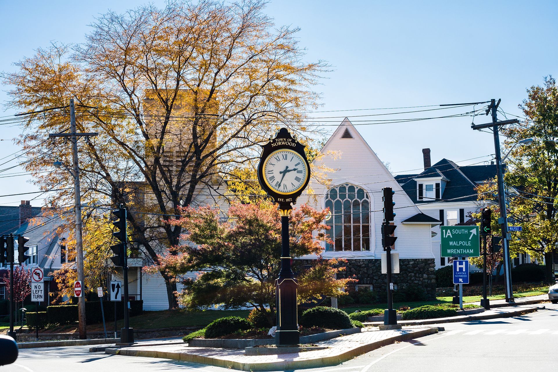 Historic town clock on a sunny street corner with autumn trees and white buildings
