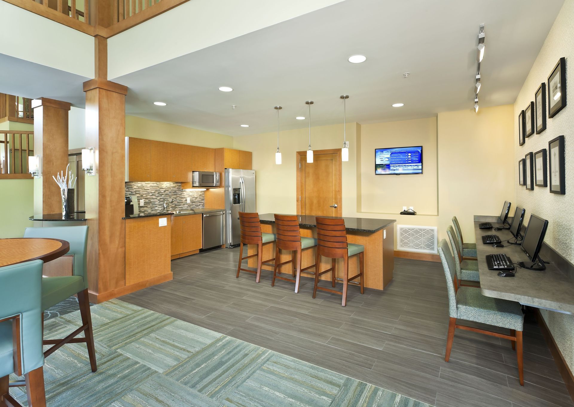 Modern community kitchen and computer station with wooden cabinetry, seating, and light tile flooring.