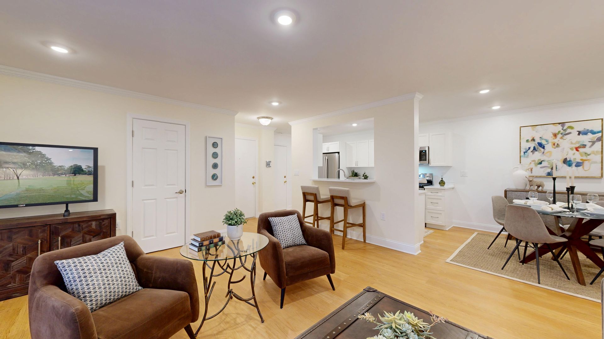 Bright open-plan living room with brown chairs, coffee table, and dining area near a white kitchen.