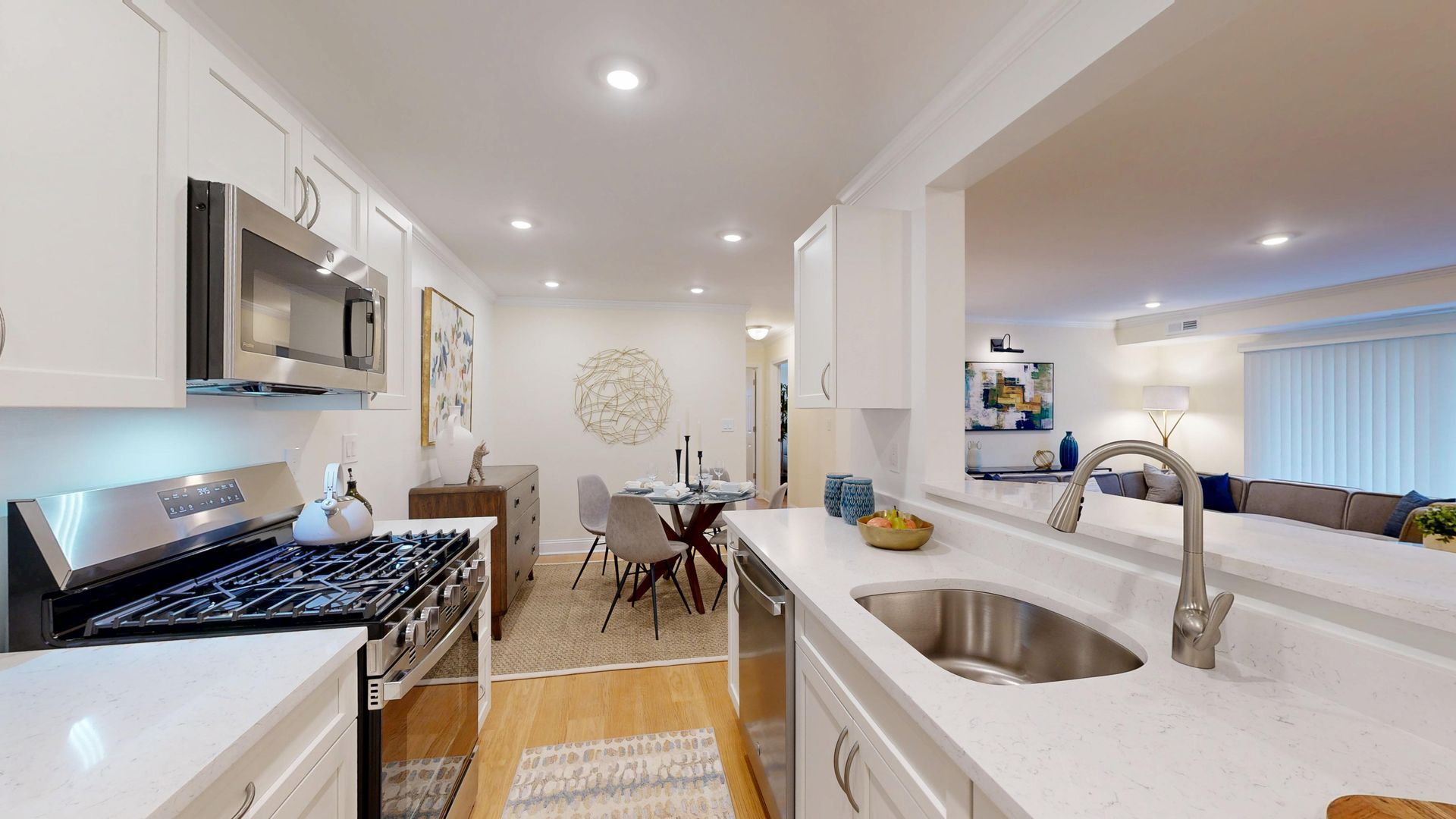 Bright modern kitchen with white cabinets, gas stove, island sink, and dining area beyond.