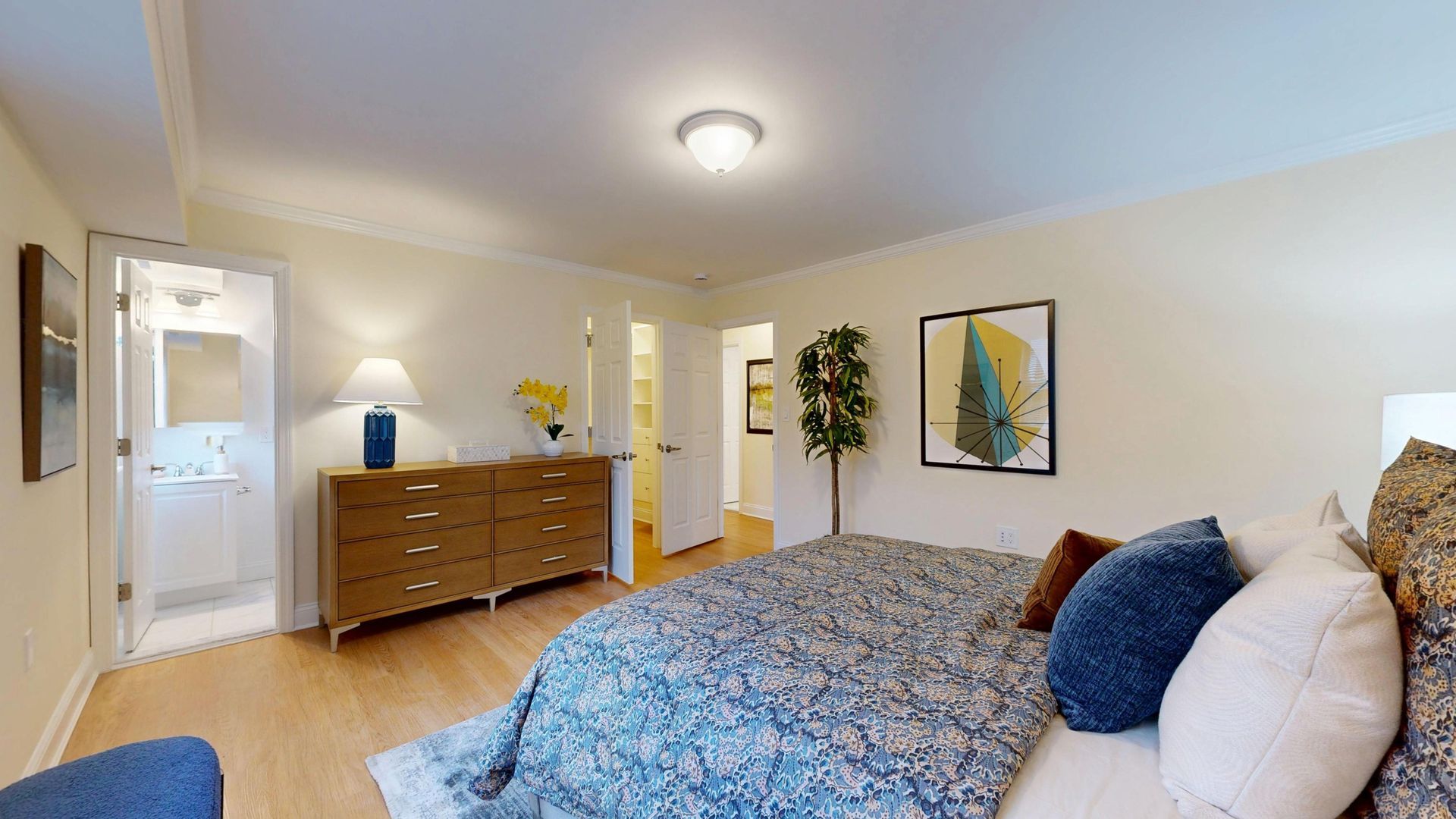 Bright bedroom with a bed, dresser, open door, and abstract wall art