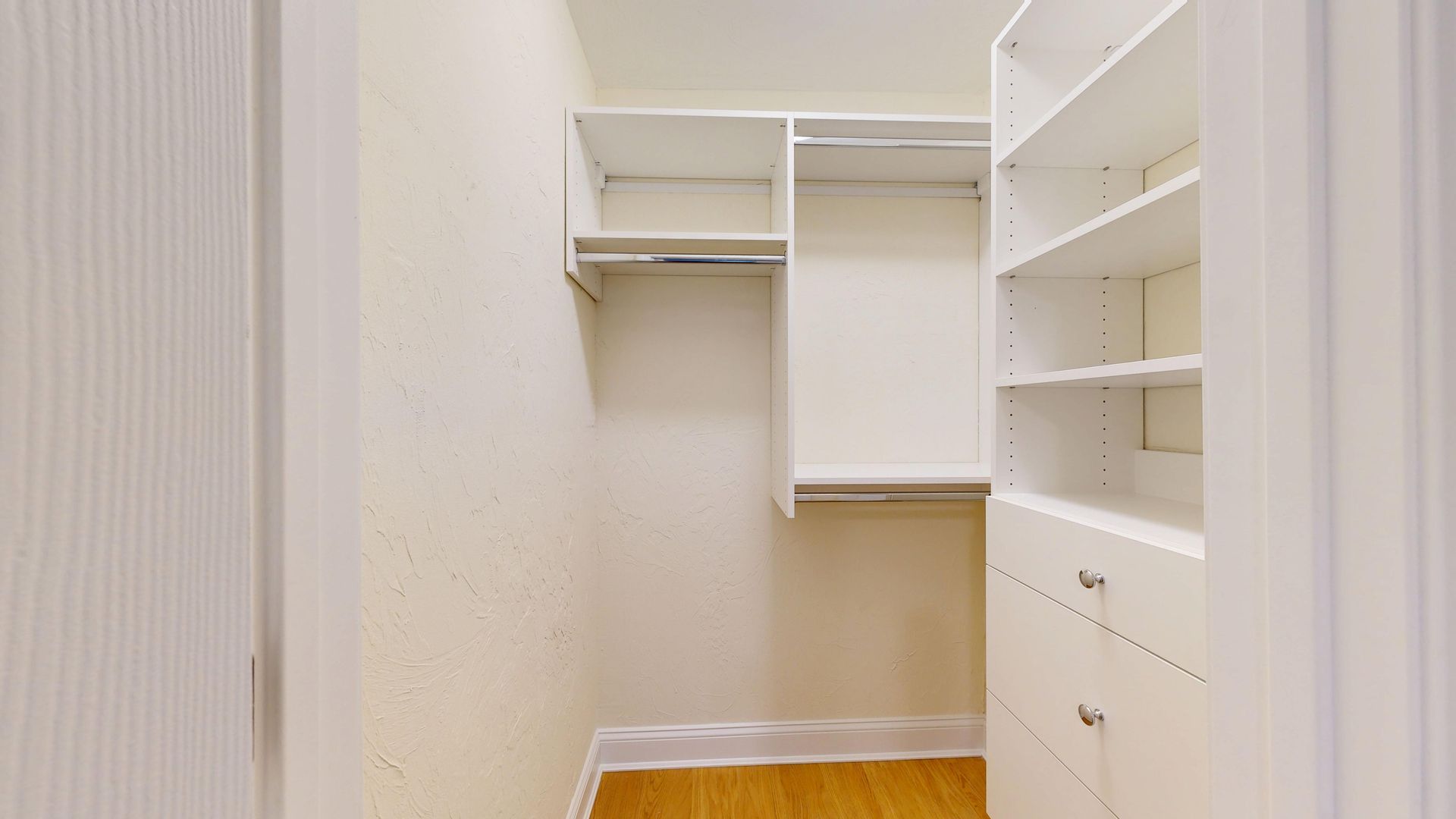 Walk-in closet with white shelves and drawers, open hanging space, and wood floor