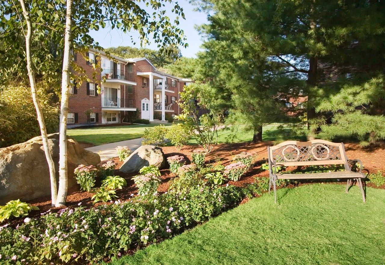 Exterior view of an apartment complex with a garden, rocks, flowers, and a bench.