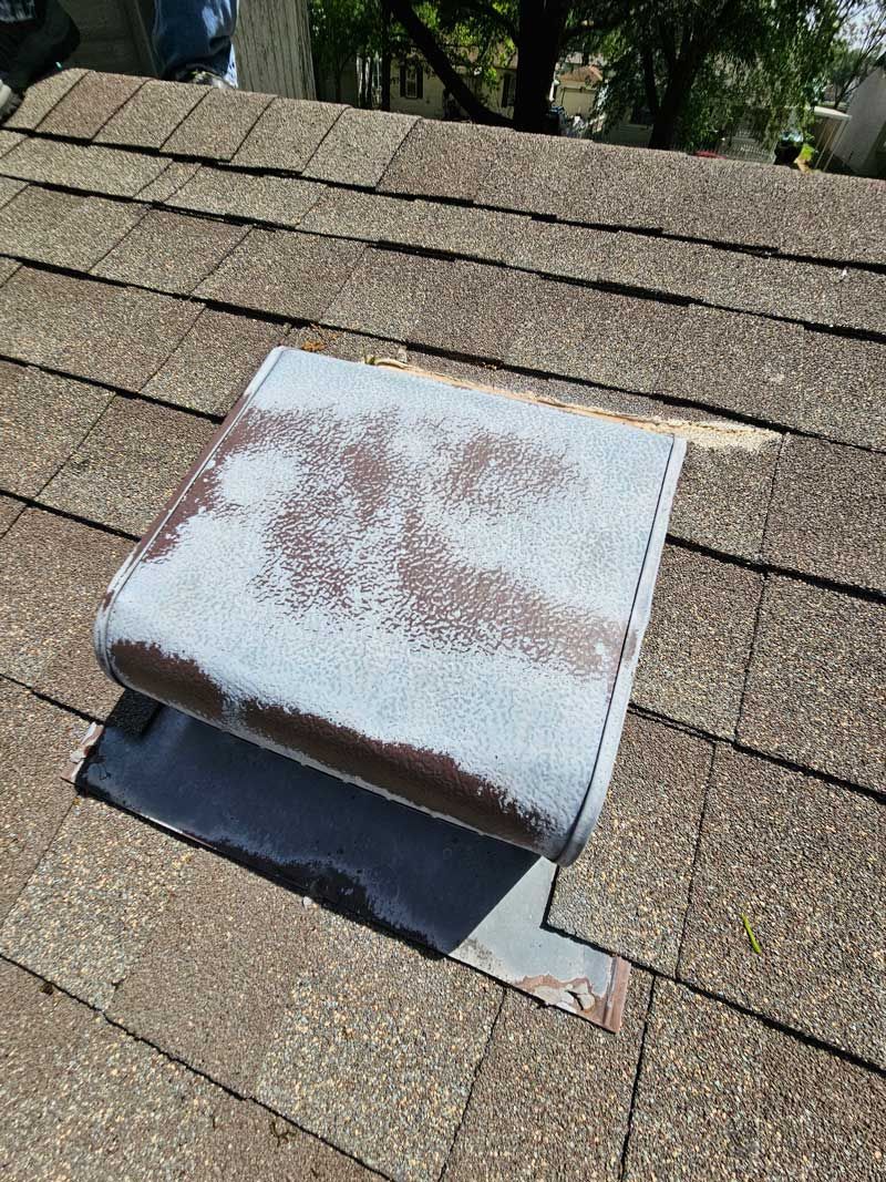 Roof vent on a shingled roof. The vent is blue with worn paint; the roof is brown.