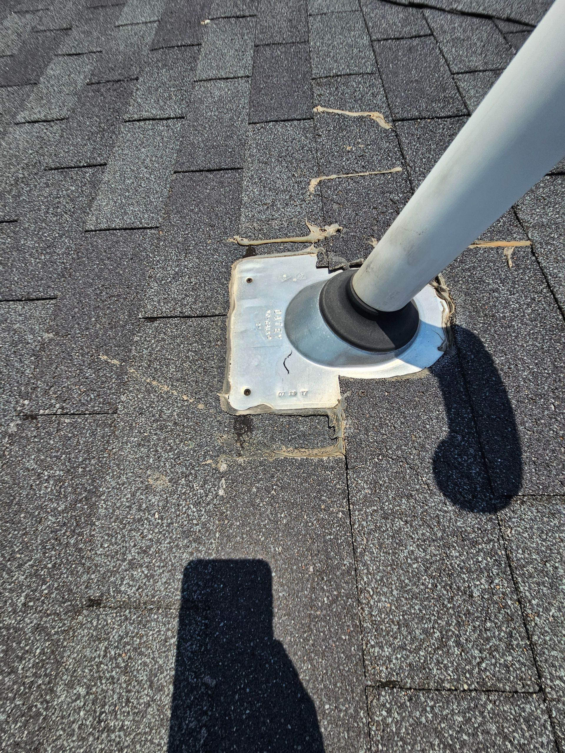 Grey asphalt shingle roof with a metal mount and white pole. Shadow cast from a person.
