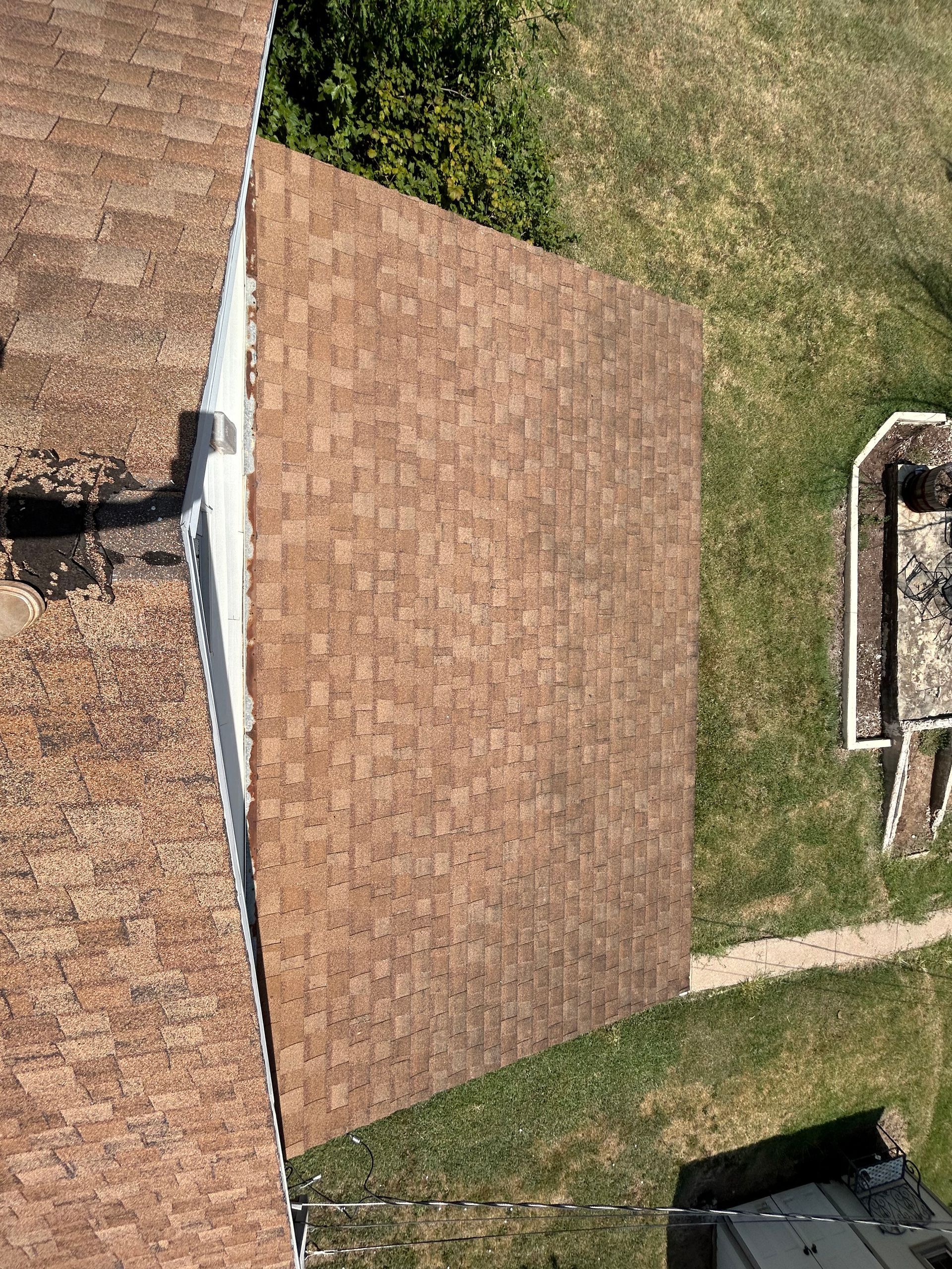 Brown shingled roof with a white trim, viewed from above, set against green grass.