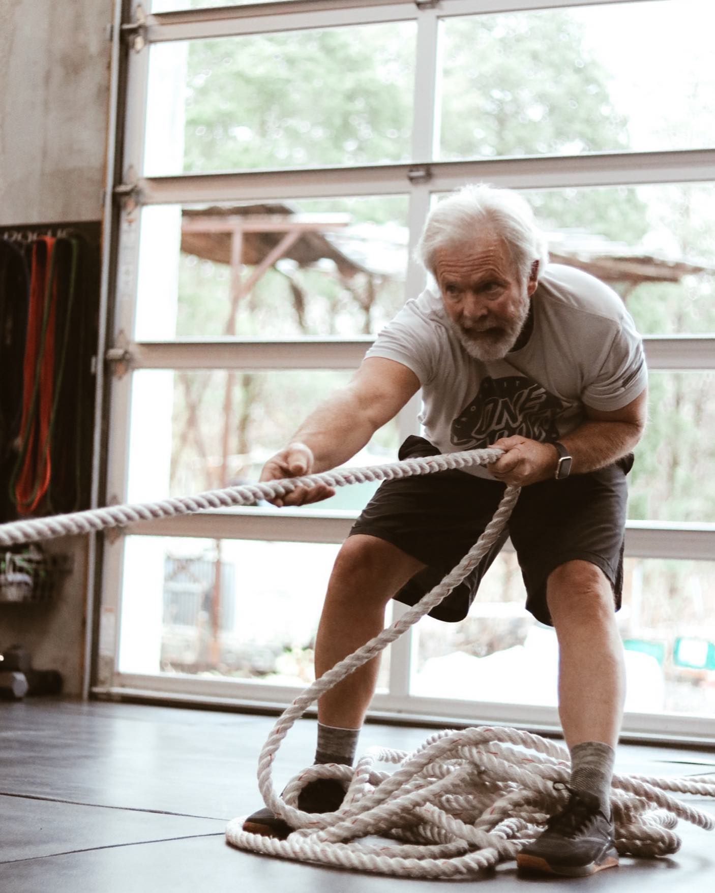 An older man is pulling a rope in a gym.