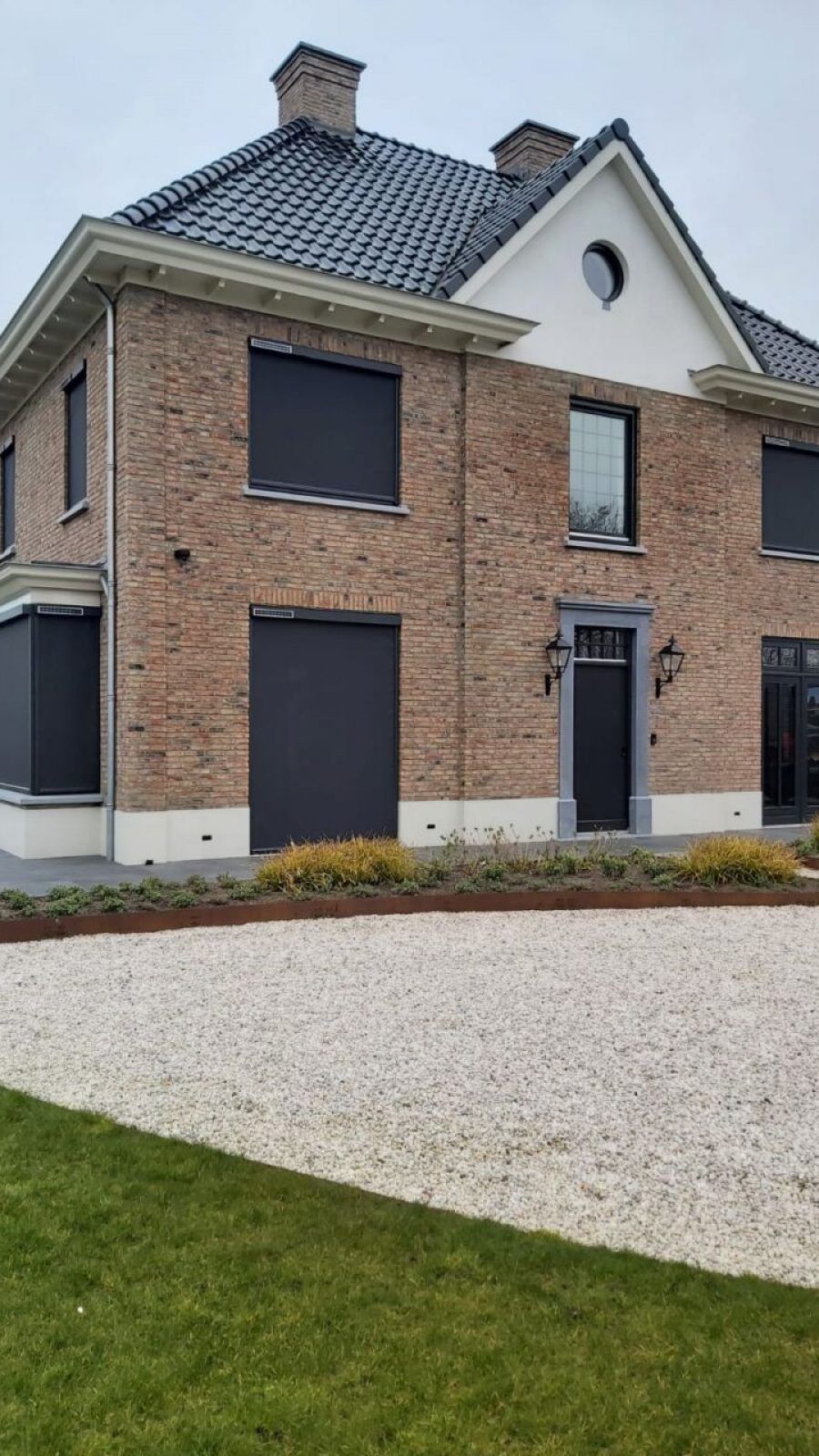 Een groot bakstenen huis met zwarte jaloezieën voor de ramen