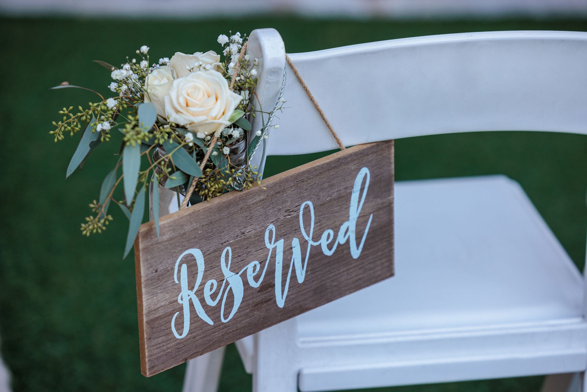 A white folding chair decorated with a floral bouquet and a rustic wooden sign that says 