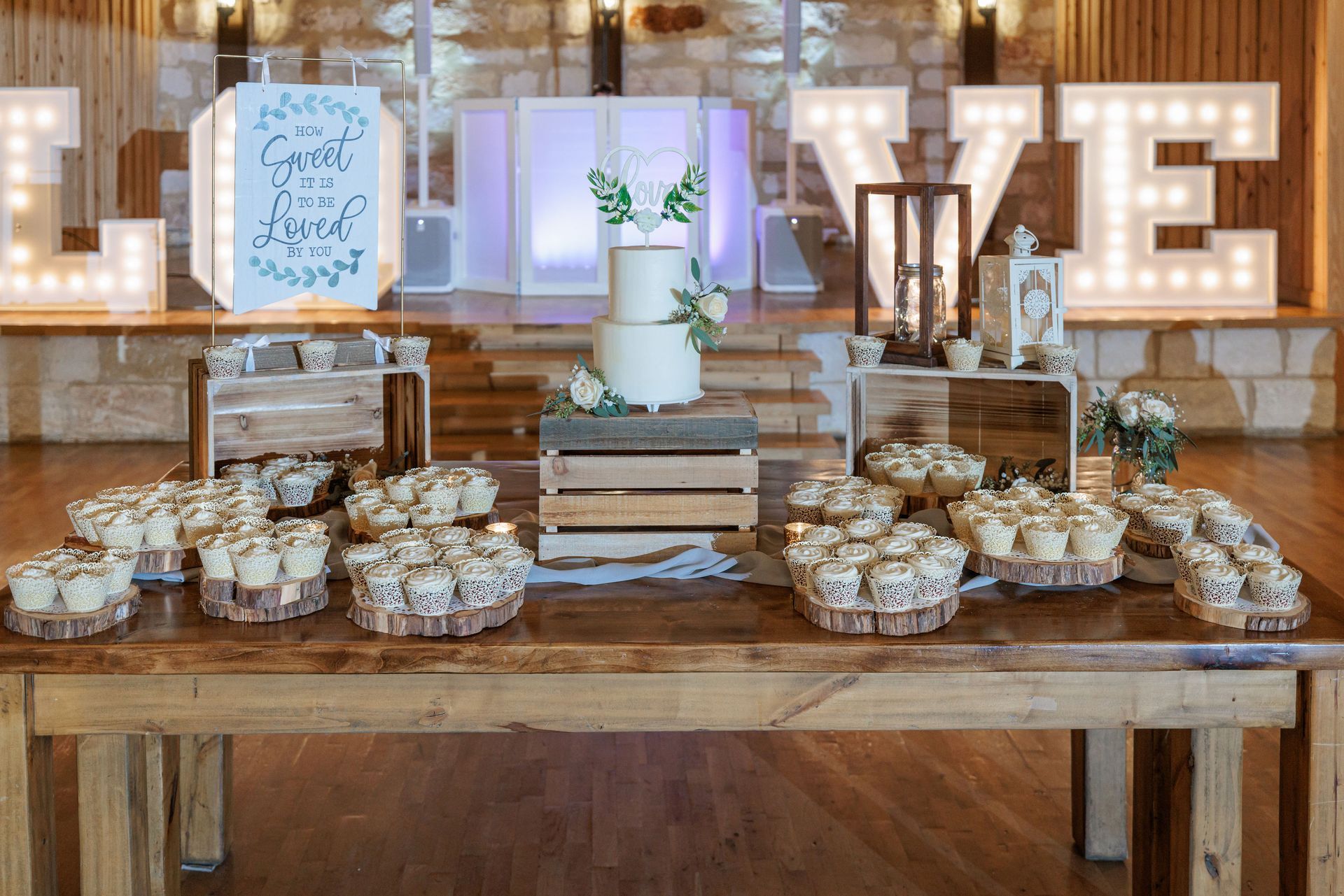 A wooden table topped with cupcakes and a wedding cake.