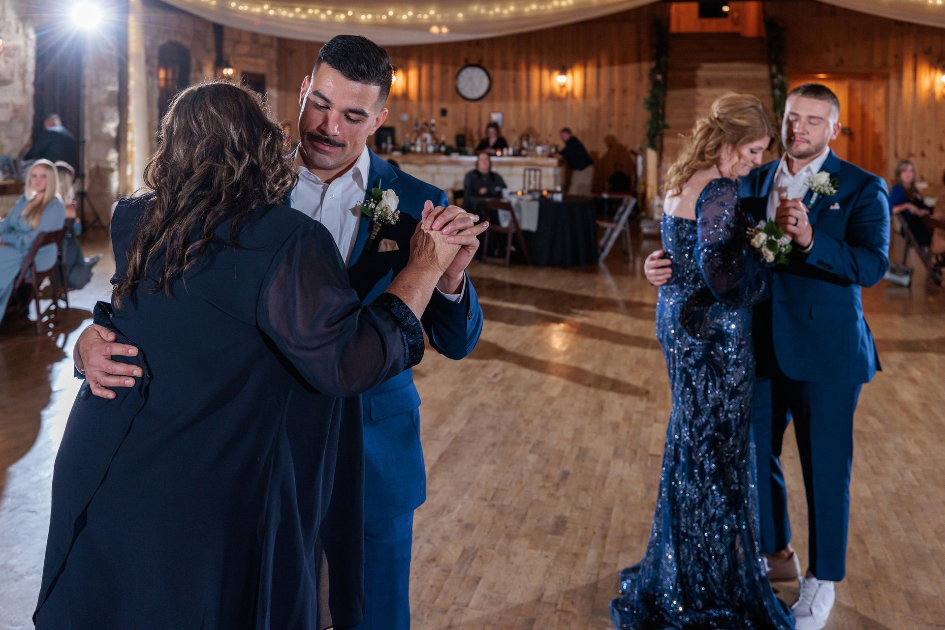 A bride and groom are dancing with their mothers at their wedding reception.