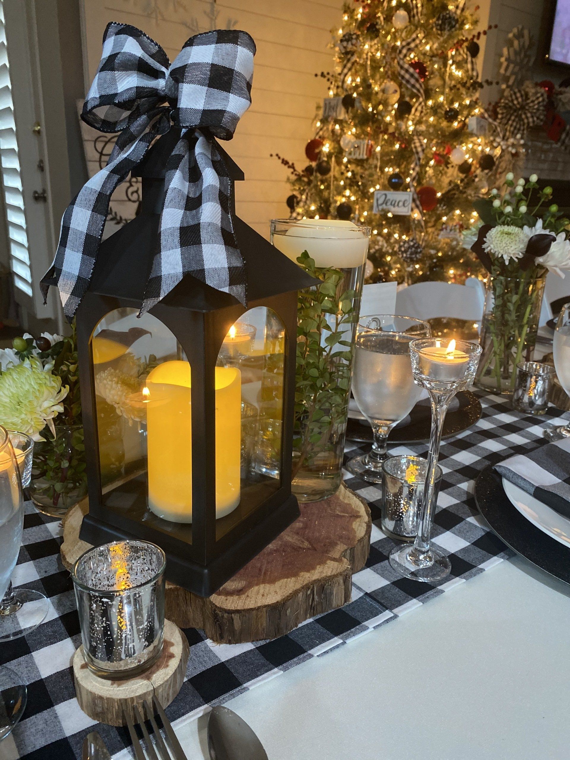 A lantern with a candle inside of it is on a table with a christmas tree in the background.
