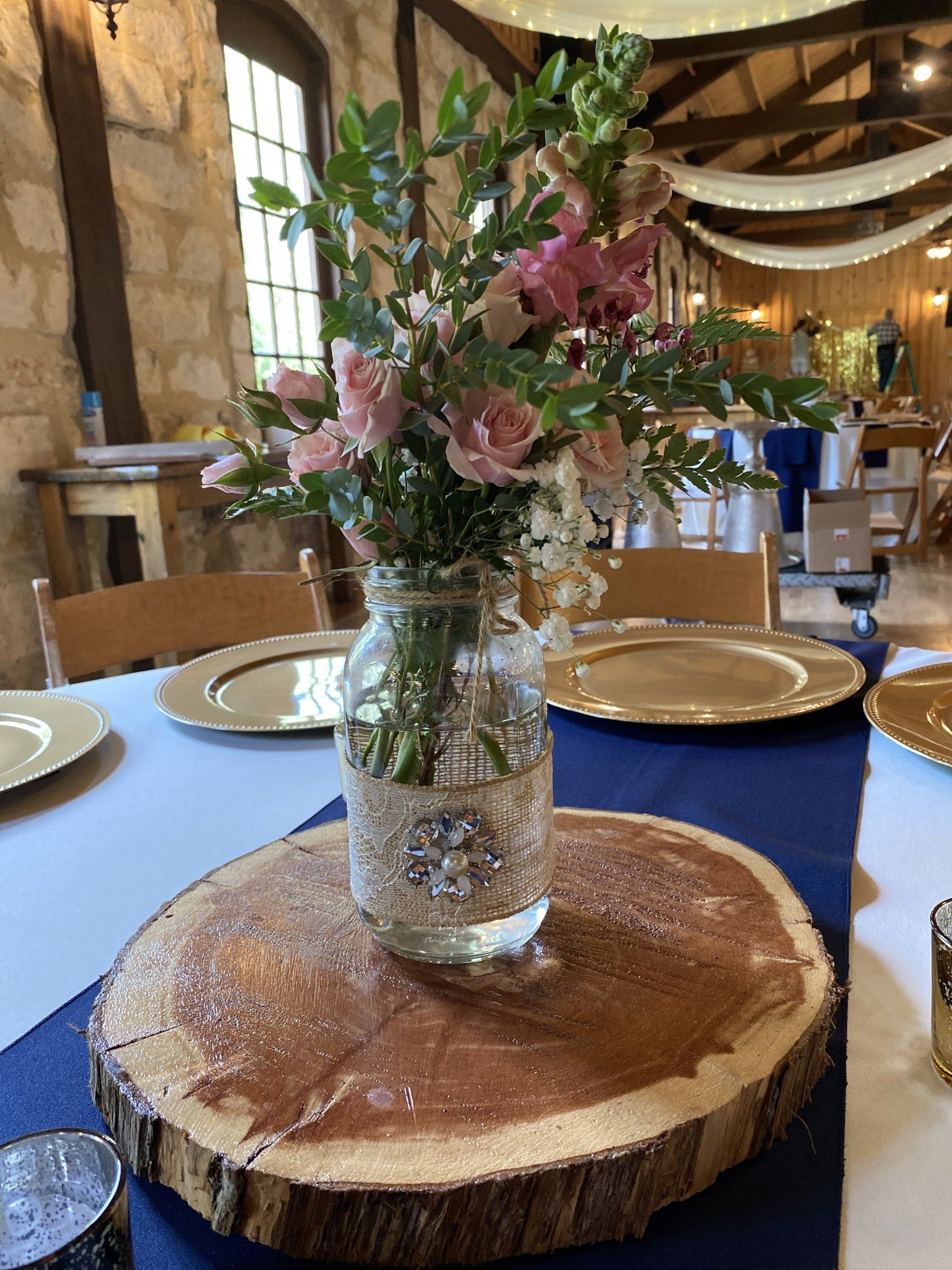 A mason jar filled with flowers sits on a wooden slice on a table.