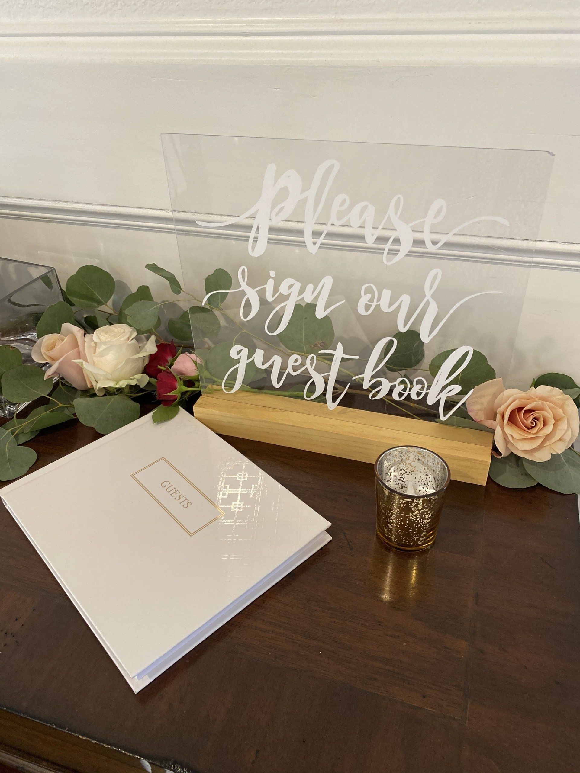 A sign that says `` please sign our guest book '' is on a table next to a guest book.