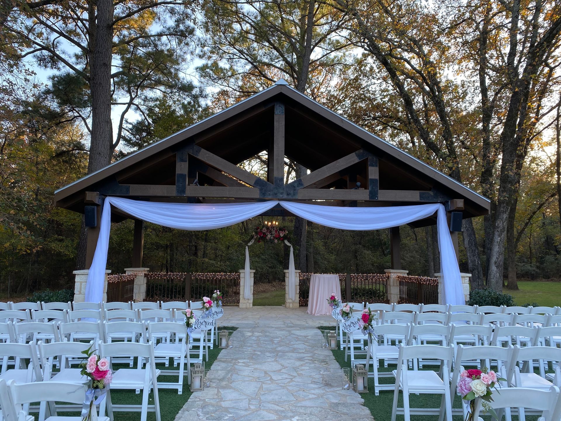 A wedding ceremony is taking place under a gazebo in the woods.