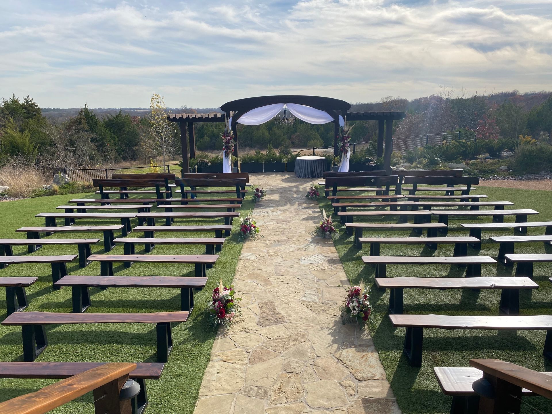 A row of wooden benches are lined up in a field for a wedding ceremony.