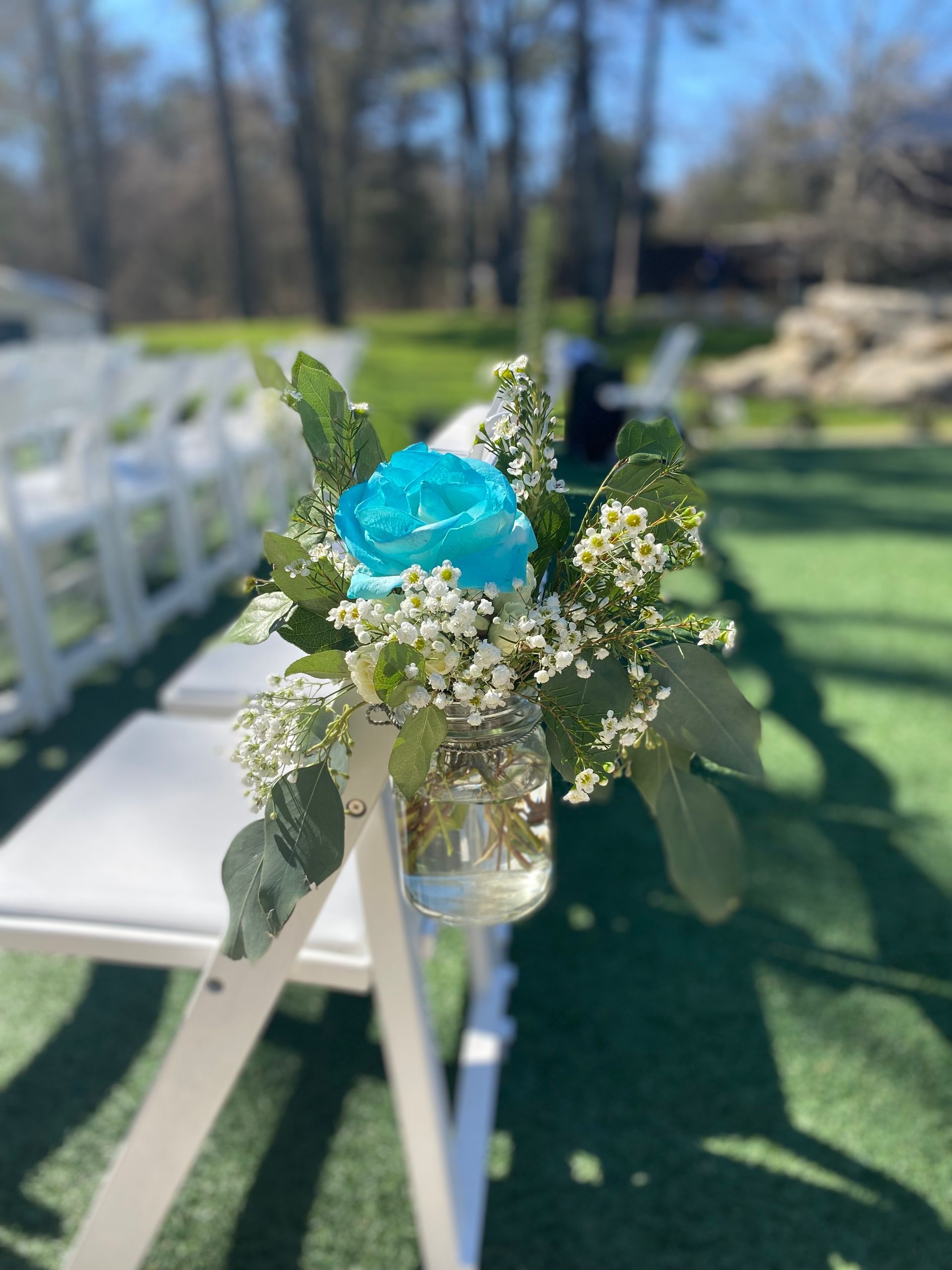 A blue rose is in a mason jar on a chair.