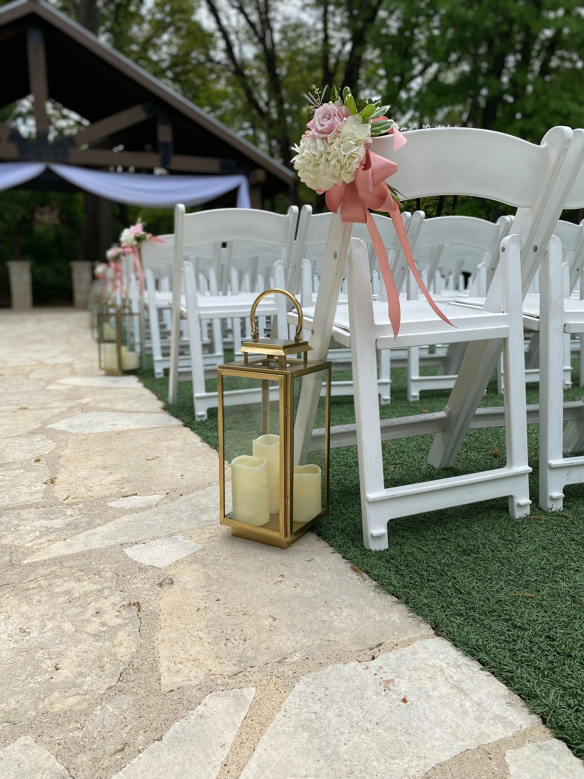 A row of white folding chairs with candles and flowers on them