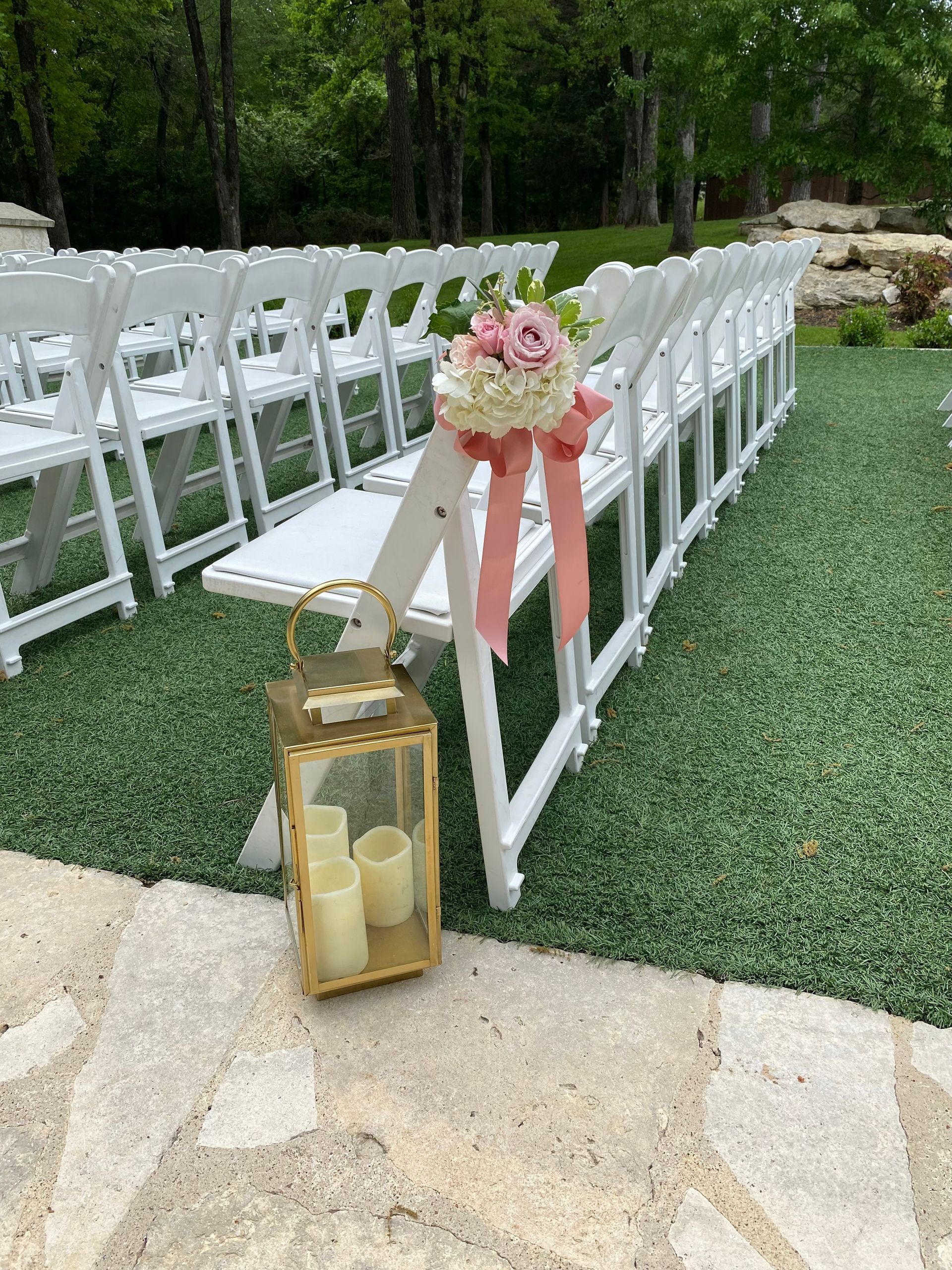 A row of white folding chairs with candles and flowers on them.
