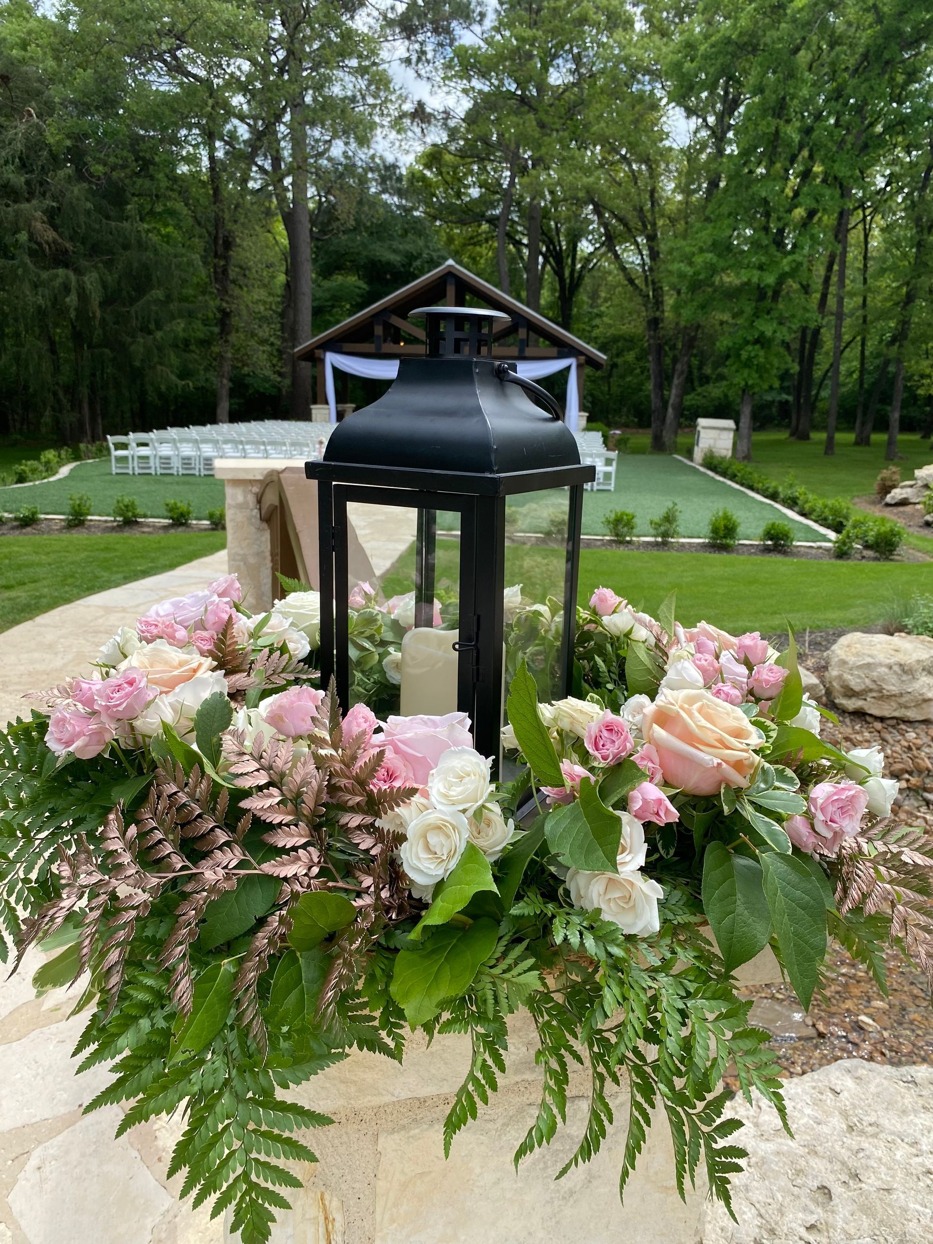 A black lantern is surrounded by pink and white flowers and ferns.