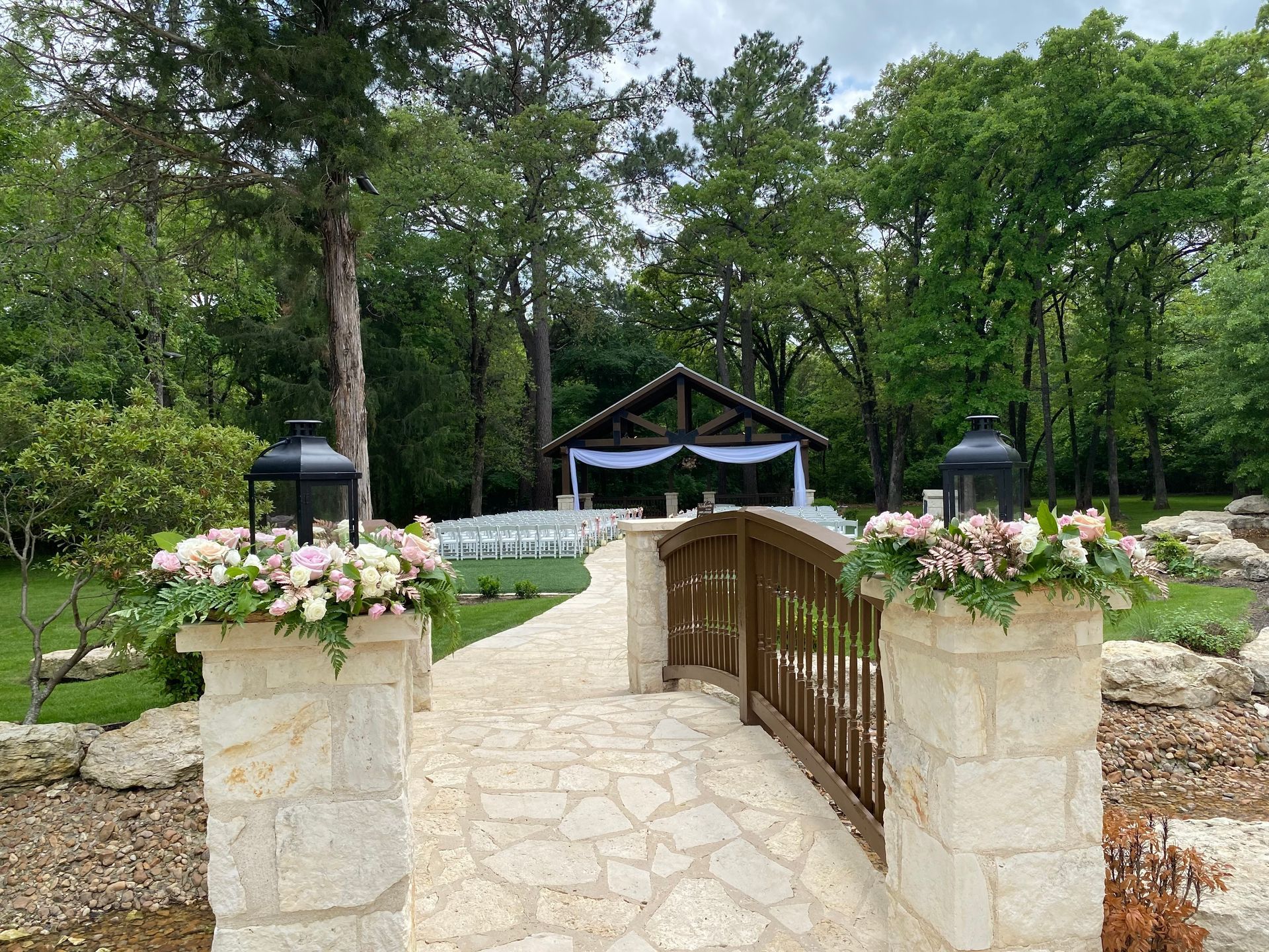 A stone bridge leading to a gazebo surrounded by trees and flowers.