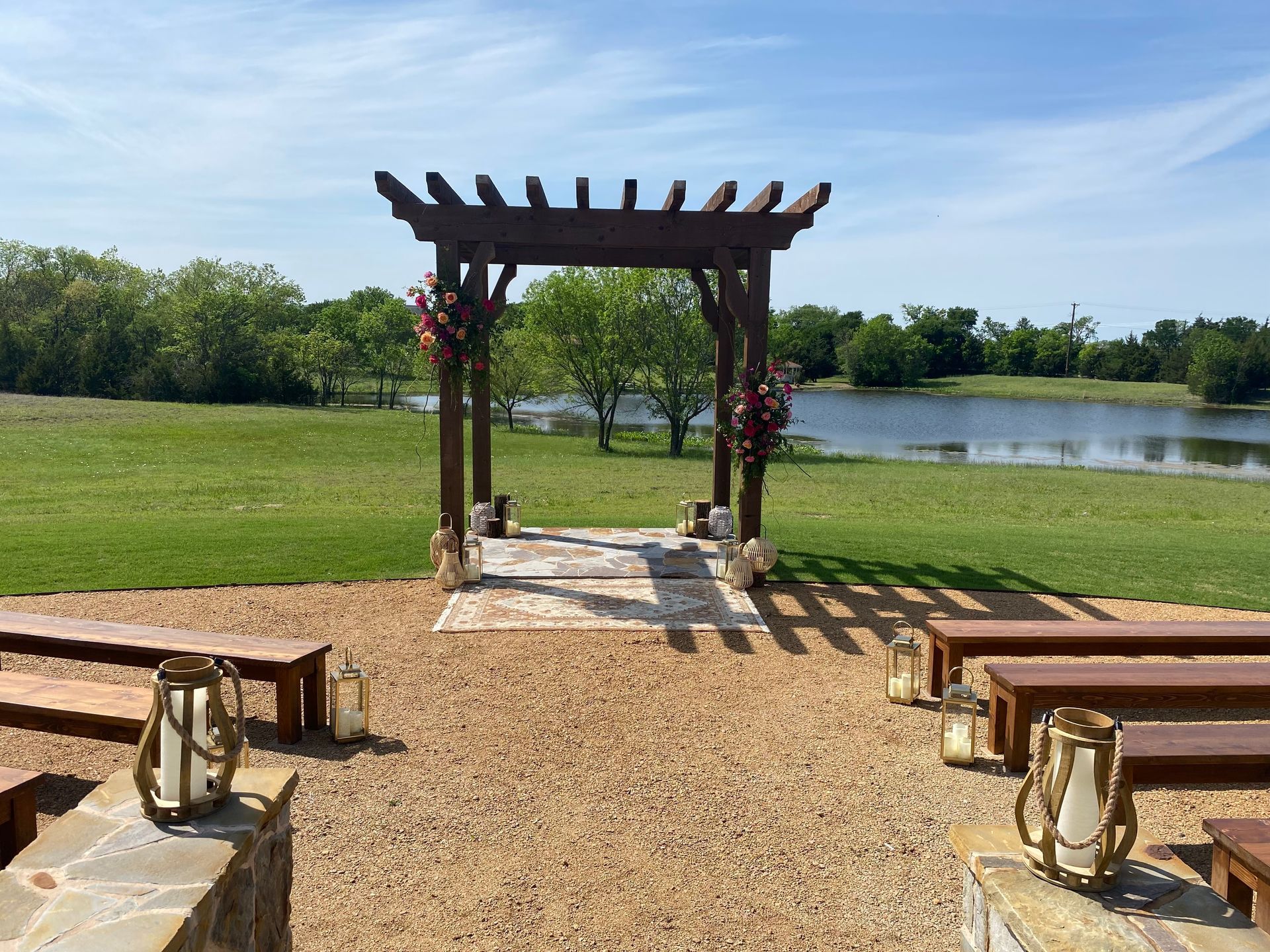A wooden archway with benches and lanterns in front of a lake.