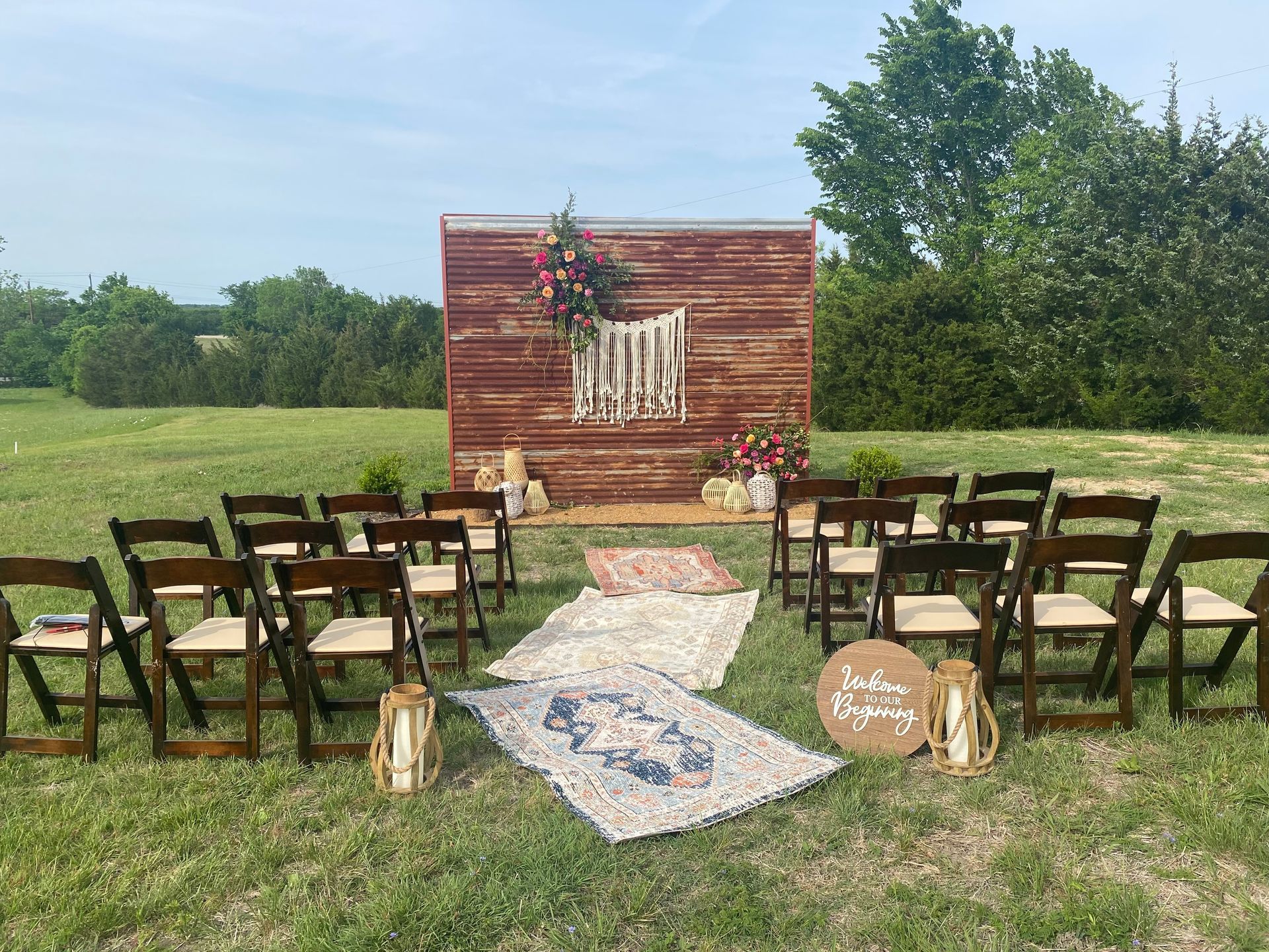 A row of folding chairs are lined up in a field in front of a wooden wall.