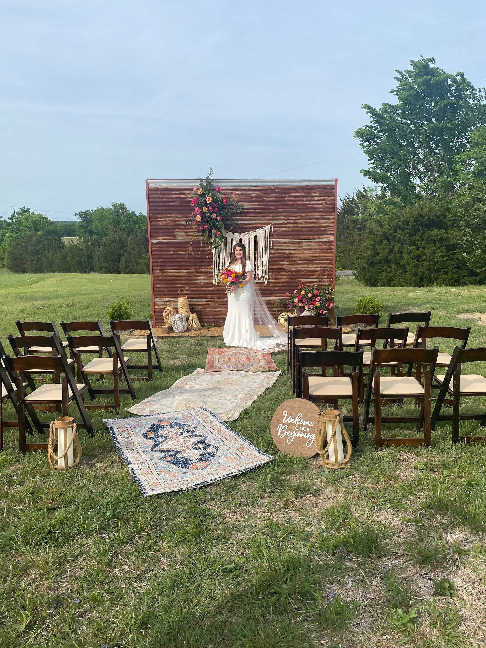 A bride and groom are standing in front of a wooden wall in a field.