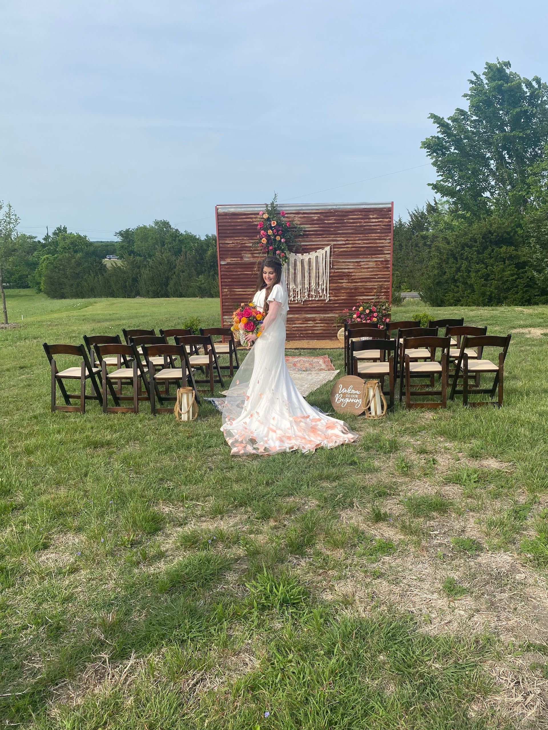 A bride in a wedding dress is standing in front of a row of chairs in a field.