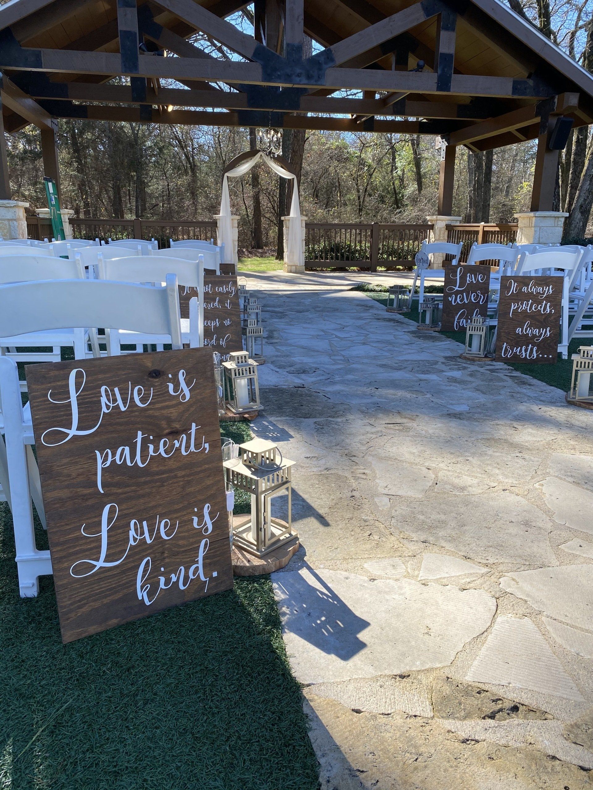 Outdoor wedding ceremony aisle lined with white chairs, decorative lanterns, and wooden signs with script lettering.