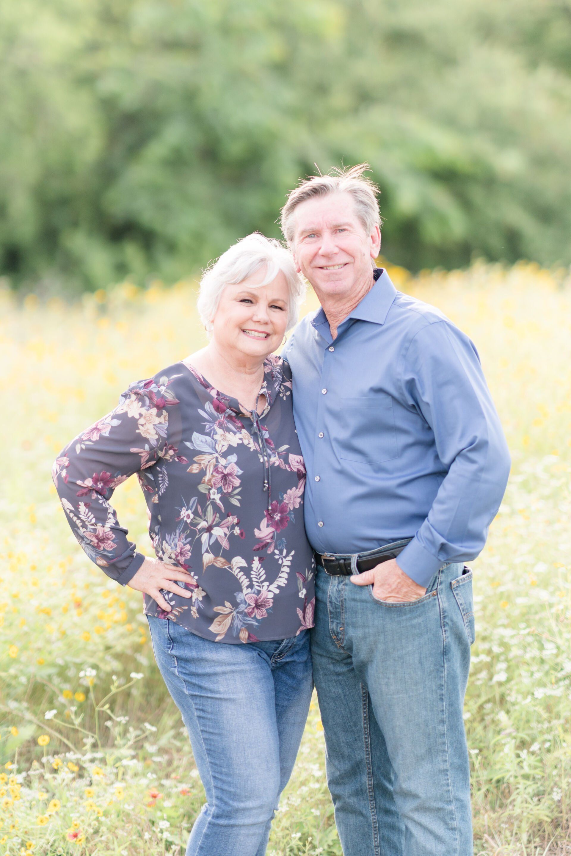 A man and a woman are posing for a picture in a field of flowers.
