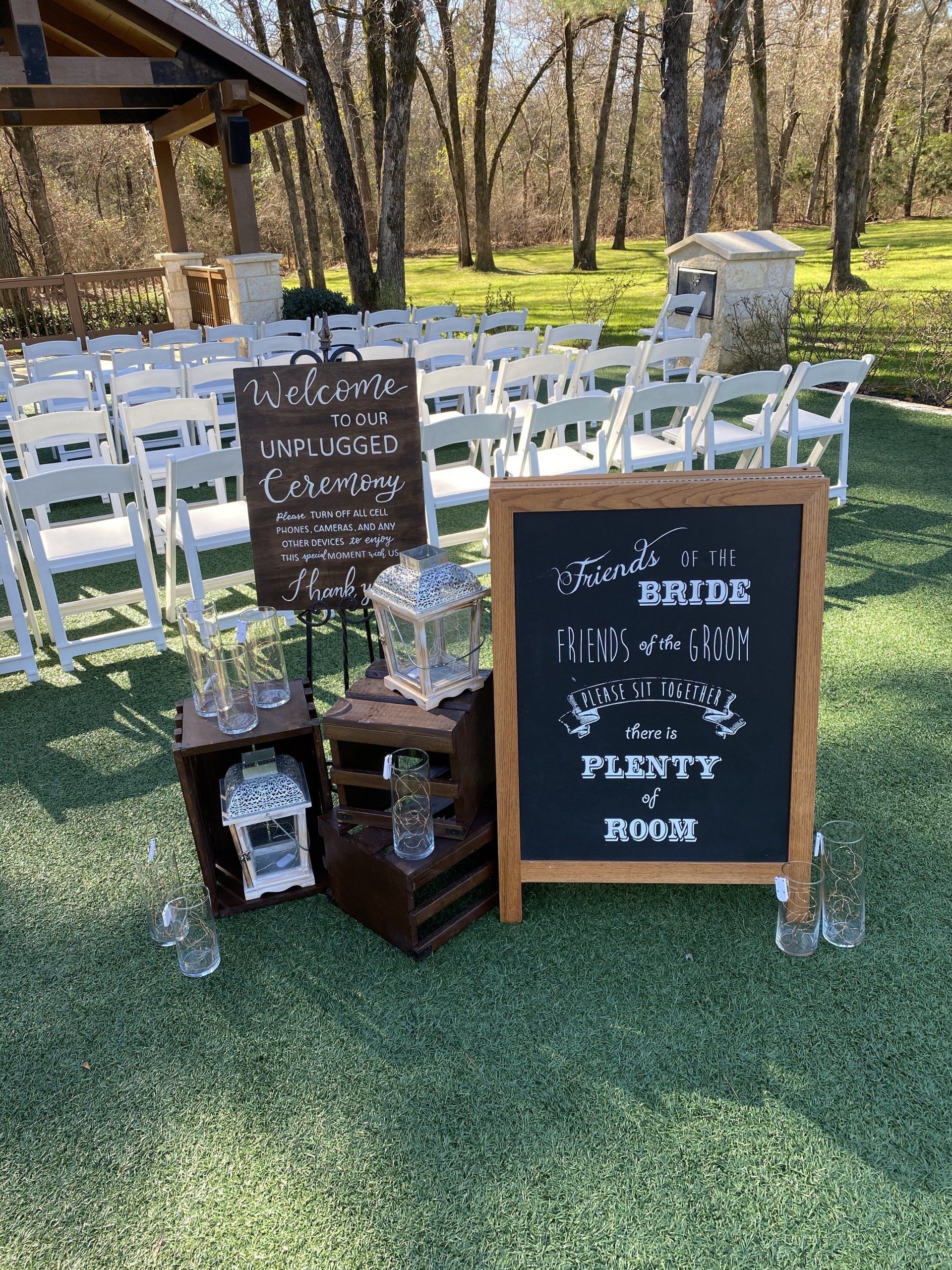 A chalkboard is sitting on top of a lush green field next to a row of white chairs.
