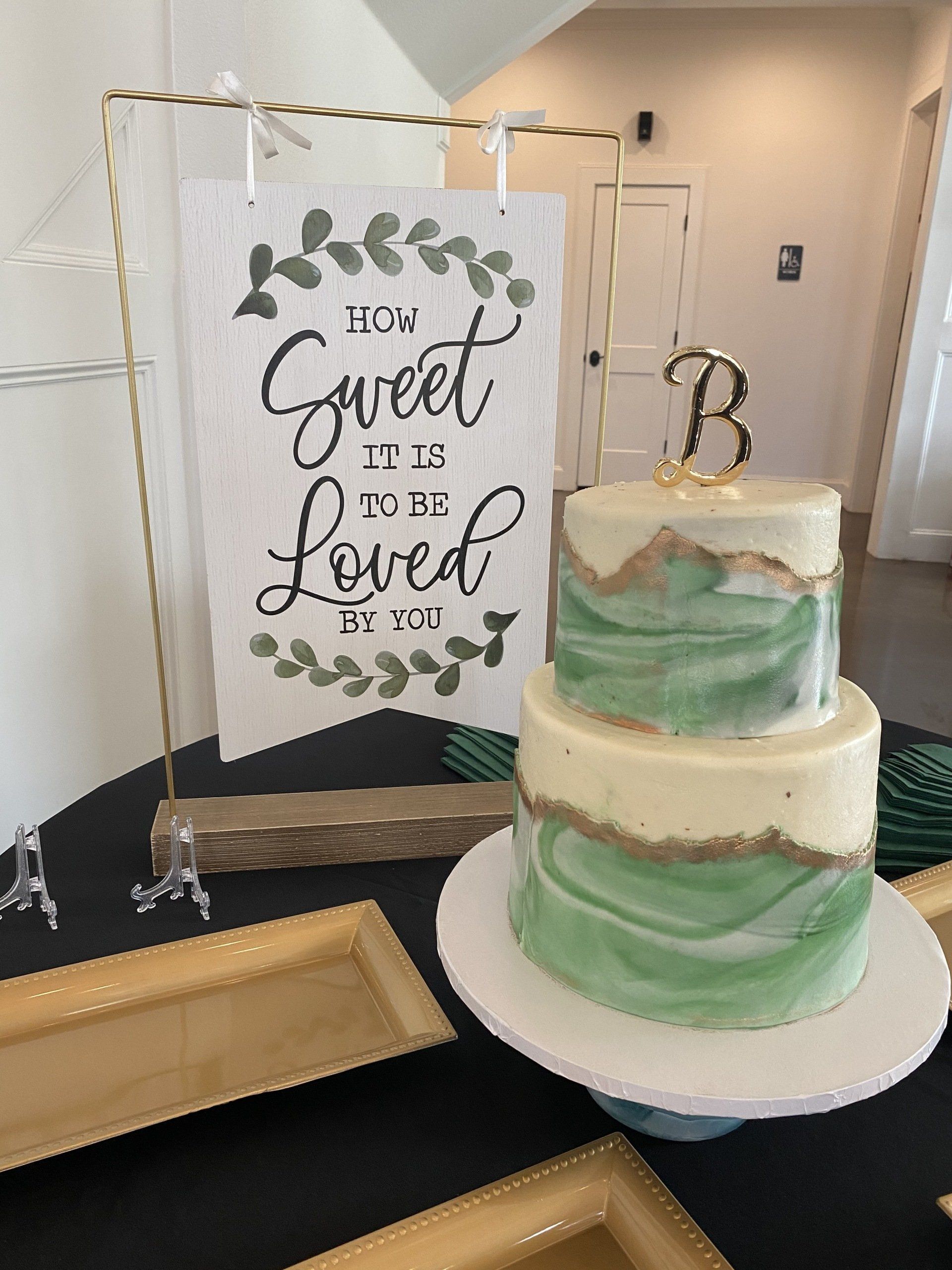 A green and white cake is sitting on a table next to a sign that says `` sweet to be loved ''.