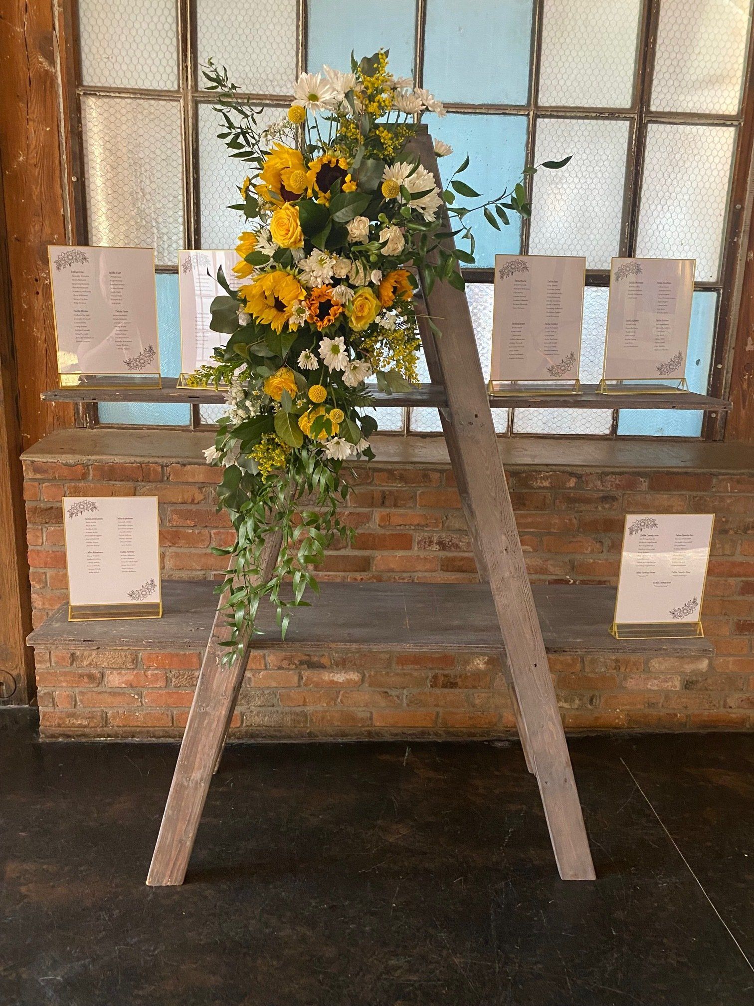 A wooden ladder with flowers on it is sitting in front of a brick wall.