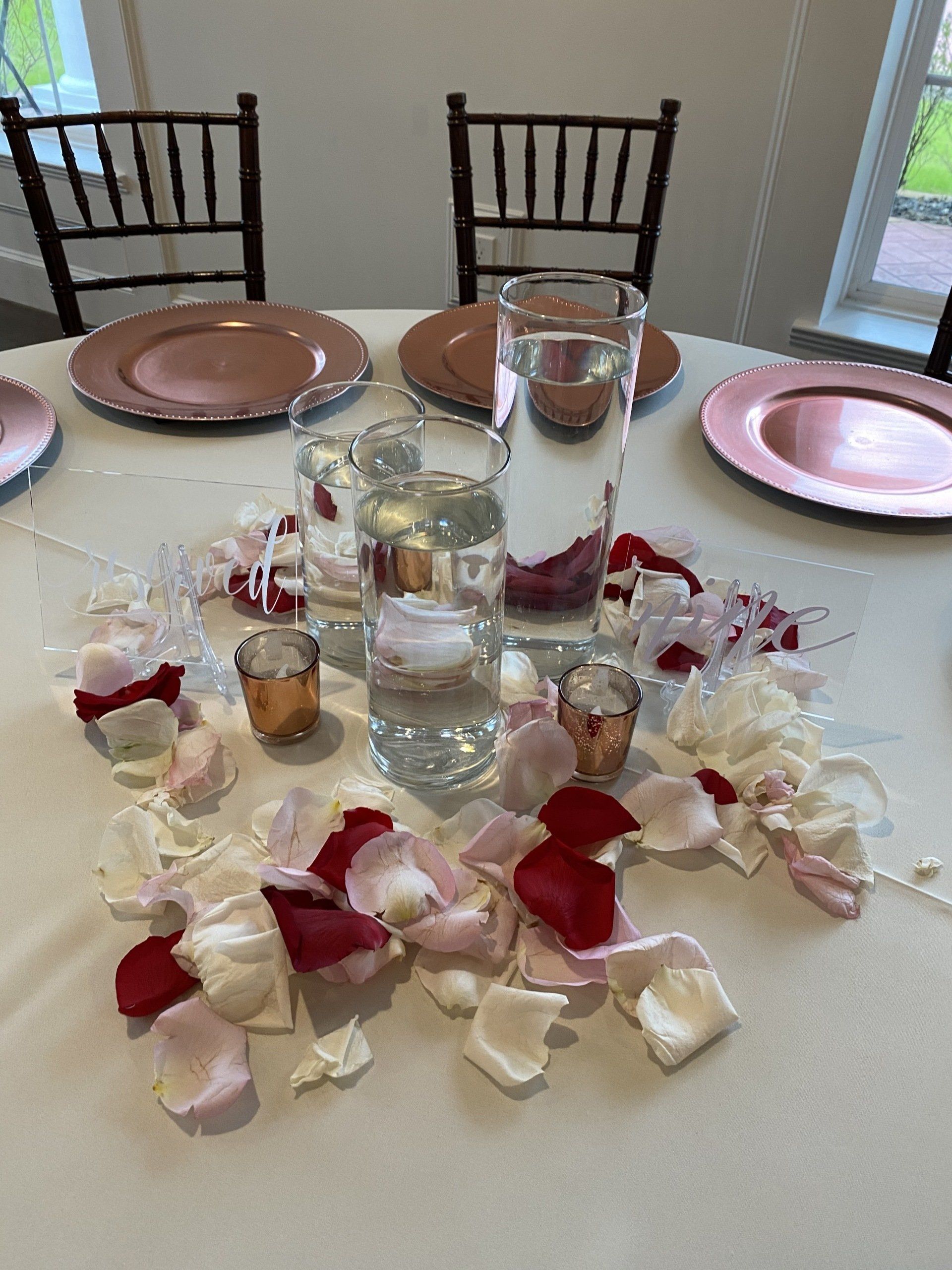 A table with plates , candles , and rose petals on it.